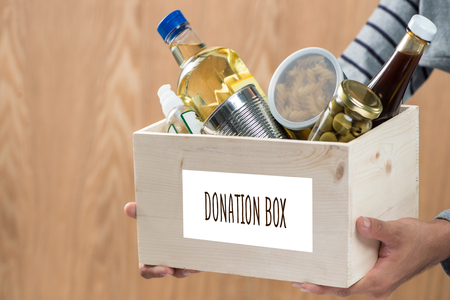 Volunteer with donation box with food stuffs on wooden backgroundの写真素材