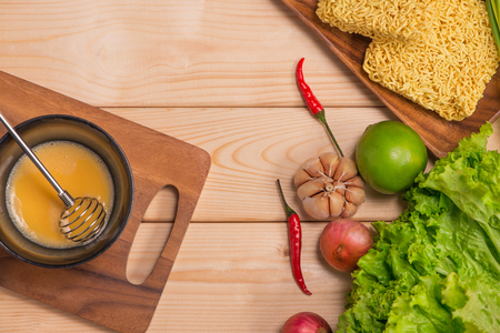 Instant noodles for cooking and eat in the dish with whipped egg and vegetables on wooden background.の写真素材