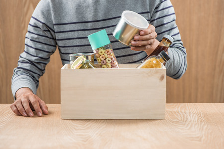 Volunteer with donation box with food stuffs on wooden backgroundの写真素材