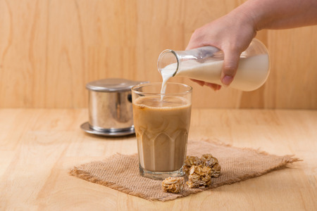 Pouring milk in to glass of coffee on a wooden table.の写真素材