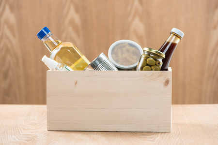 Volunteer with donation box with food stuffs on wooden backgroundの写真素材