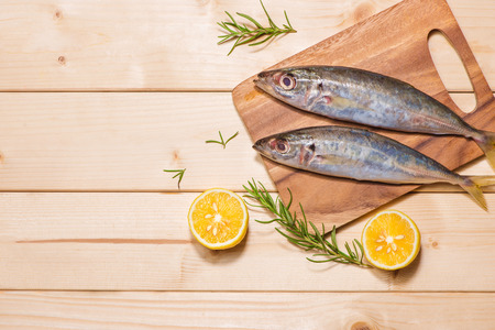 Fish dish cooking with various ingredients. Fresh raw fish decorated with lemon slices and herbs on wooden table.の写真素材