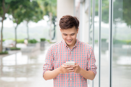 Asian young man using smart phone outdoorの写真素材