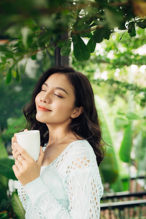 Pretty vietnamese woman enjoying her morning coffee on a verandaの写真素材