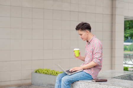 Portrait of a happy young man sitting on the city stairs with laptopの写真素材