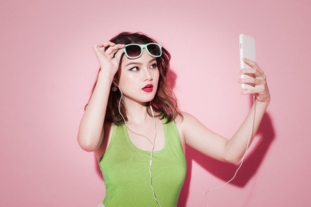 Stylish asian woman taking selfie photo on pink background.の写真素材