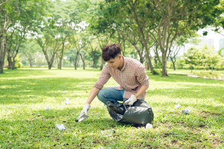 Young asian man in yellow rubber gloves putting household waste into small bin bagの写真素材