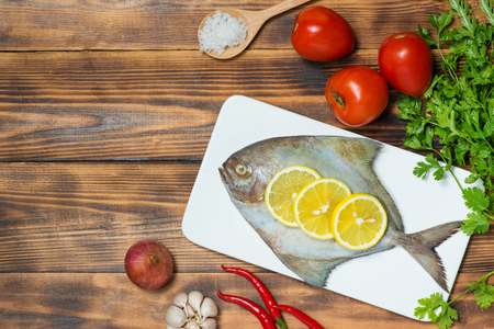 Fish dish cooking with various ingredients. Fresh raw fish decorated with lemon slices and herbs on wooden table.の写真素材