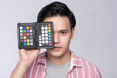 Young asian photographer holding color checker card, while working in studioの写真素材