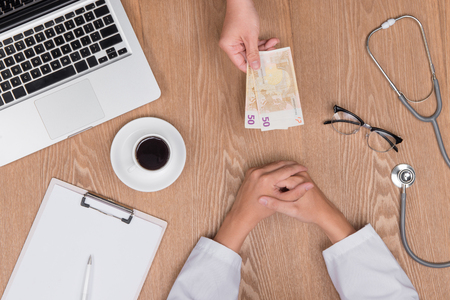 Cropped image of young doctor in white coat talking money from his patient while working in officeの写真素材