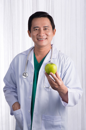 Nurse or male doctor giving an apple smiling. Health care concept isolated on white background.の写真素材