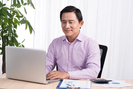 Business asian man sitting at his desk working on a computer and looking concentratedの写真素材