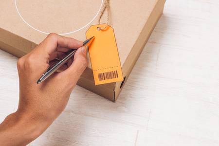 Male hand writing on luggage tag on brown paper parcel