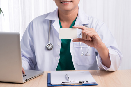 Smiling doctor sitting at his desk in medical office showing namecardの写真素材