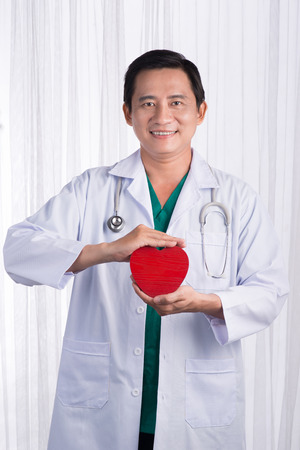 Asian male doctor with stethoscope holding heart, isolated on white backgroundの写真素材