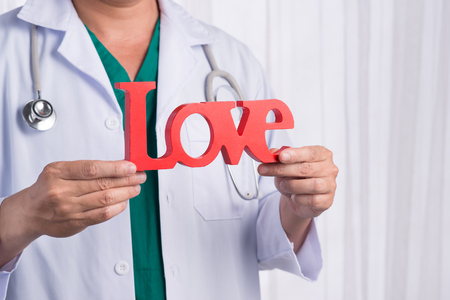 Asian male doctor with stethoscope holding LOVE letters, isolated on white backgroundの写真素材