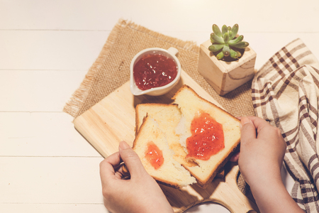 Asian woman eating bread with strawberry jam for breakfast. Focus on hands.の写真素材