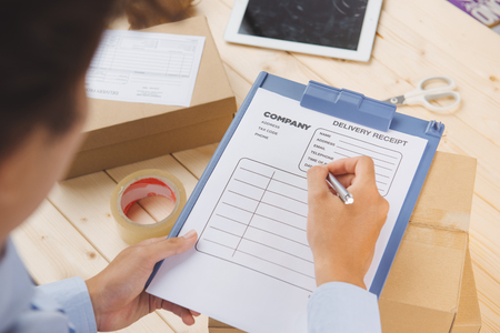 Close-up of deliveryman making notes in delivery receipt at tableの写真素材