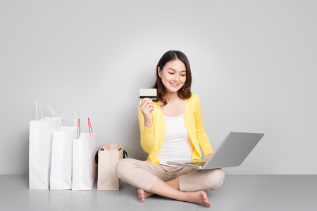 Young asian woman shopping online at home sitting besides row of shopping bagsの写真素材
