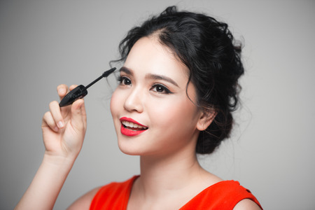 Close-up portrait of beautiful girl touching black mascara to her lashesの写真素材