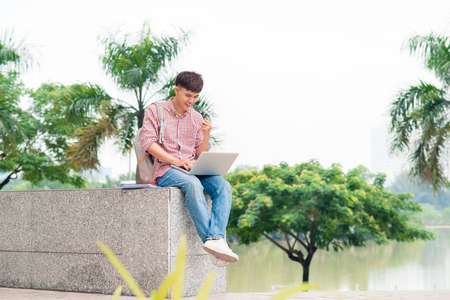 Smiling college student sitting on staircase with laptop outdoorsの写真素材