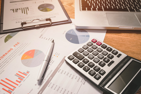 Business graphs and charts on a wooden desk with a calculator, coffee mug and penの写真素材