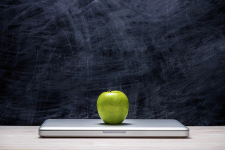 Apple on laptop on table in front of chalkboard.の写真素材