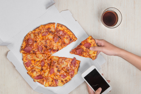 Hands ordering pizza with a device over a wooden workspace tableの写真素材