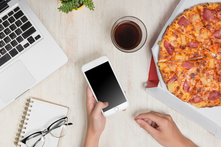 Hands ordering pizza with a device over a wooden workspace tableの写真素材