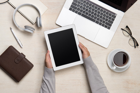 Male hands holding digital tablet with laptop on a wooden desktopの写真素材