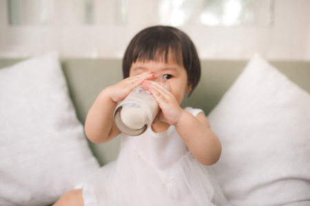 Cute baby girl drinking milk with milk mustache at homeの写真素材