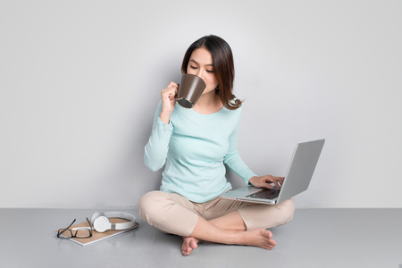 Happy casual beautiful asian woman working on a laptop sitting on floor at home.の写真素材
