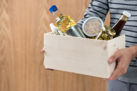 Volunteer with donation box with food stuffs on wooden backgroundの写真素材