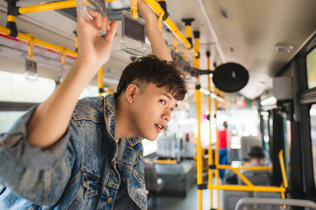Asian man taking public transport, standing inside bus.