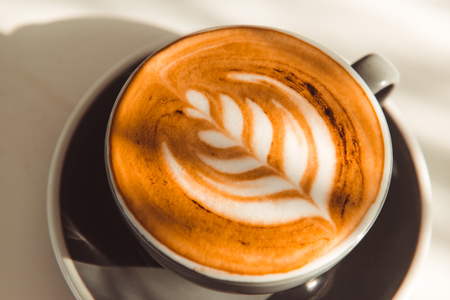Cup of art latte or cappuccino coffee on table with sunlightの写真素材