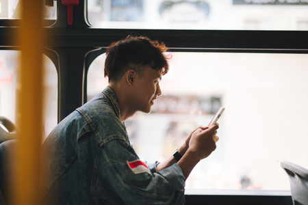 Handsome asian man sitting in city bus and typing a message on the phone.の写真素材