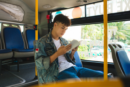 Young man sitting in city bus and reading a book.の写真素材