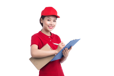 Beautiful young delivery woman in red t-shirt and cap smiling, holding a folder and making notes, on white backgroundの写真素材