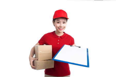 Beautiful young delivery woman in red t-shirt and cap smiling, holding a folder and making notes, on white backgroundの写真素材