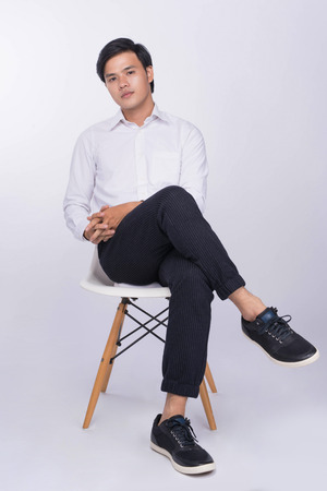 Full length of young handsome man in a white shirt  sitting on a chairの写真素材
