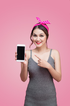 Beautiful young asian woman with pin-up make-up and hairstyle over pink background with mobile phoneの写真素材