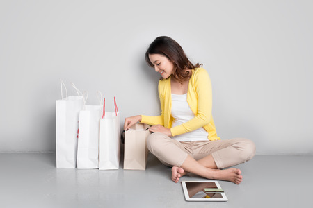 Young asian woman shopping online at home sitting besides row of shopping bagsの写真素材