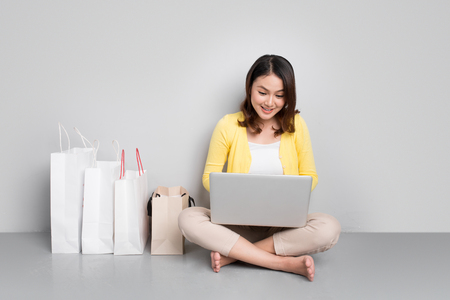Young asian woman shopping online at home sitting besides row of shopping bagsの写真素材