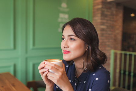 Portrait of happy young business woman with mug in hands drinking coffee in the morning at restaurantの写真素材