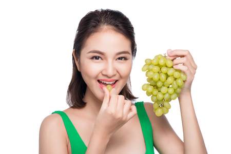 Young beautiful asian woman eating fresh grapes isolated on white backgroundの写真素材