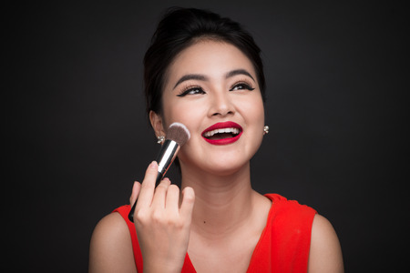 Cosmetic powder brush. Asian woman applying blusher on her cheeks with perfect make-up and red lipsの写真素材