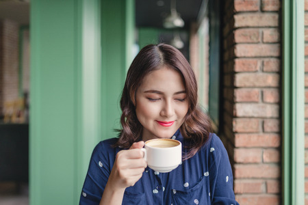 Portrait of happy young business woman with mug in hands drinking coffee in the morning at restaurantの写真素材