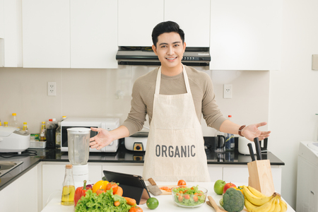 Handsome vietnamese man cooking at home preparing salad in kitchen.の写真素材