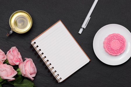 Snow skin mooncake and tea cup with flowers on dark background. Open notebook with copy-space.の写真素材