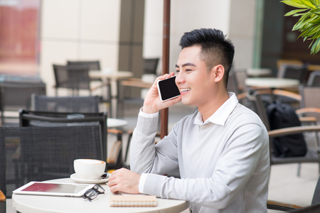 Handsome man drinking coffee and talking on the phone at coffee shopの写真素材